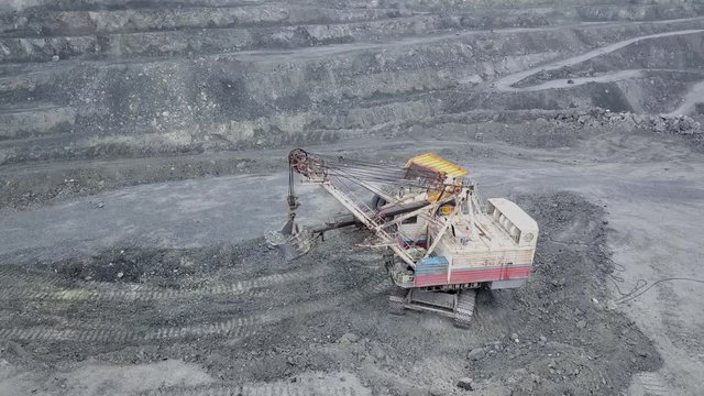 Top view of excavator in open pit. Excavator falls asleep rubble in dumper on outdoor quarry in extraction of minerals. Concept of extraction of minerals