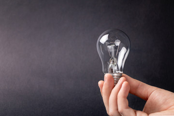 A man's hand holds a light bulb on a dark background
