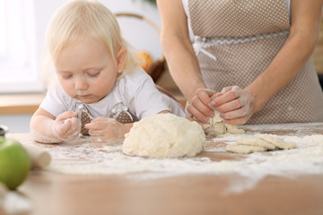 Little girl and her blonde mom in beige aprons  playing and laughing while kneading the dough in kitchen. Homemade pastry for bread, pizza or bake cookies. Family fun and cooking concept