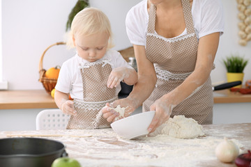 Little girl and her blonde mom in beige aprons  playing and laughing while kneading the dough in kitchen. Homemade pastry for bread, pizza or bake cookies. Family fun and cooking concept