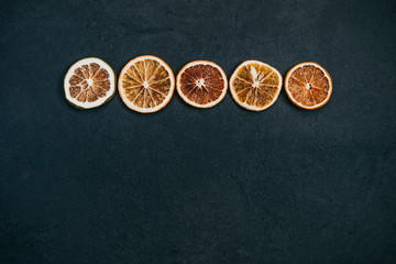 Slices of dried orange orranged in a line on a black background.