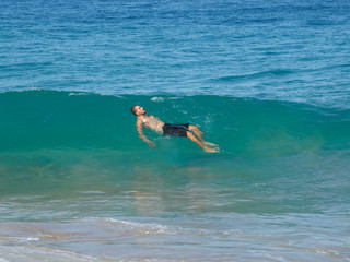 A man swims on a turquoise wave in the ocean.