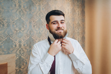 Portrait of a stylish bearded groom. Young man puts shirt on in room. Morning groom. Cool emotions....