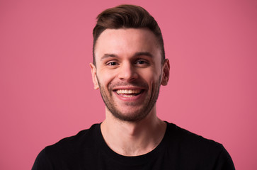 Happy handsome young man portrait in black t-shirt isolated on pink wall