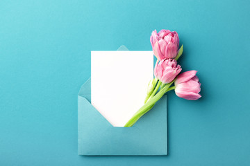 Three pink tulips in turquoise envelope on turquoise background. Mockup with white card. Flat lay,...