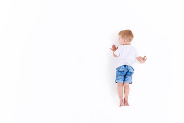 Little caucasian boy in white clothes on white wall, white background isolated. View from the back 