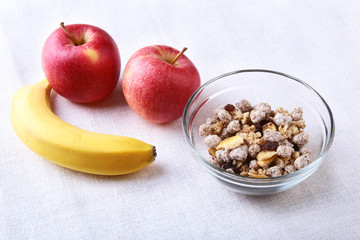 Healthy breakfast with banana, apple and Fresh granola, muesli in bowl on textile background. Top view.