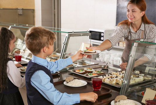 Woman giving plate with healthy food to boy in school canteen