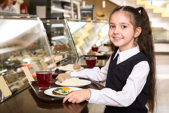 Cute girl near serving line with healthy food in school canteen