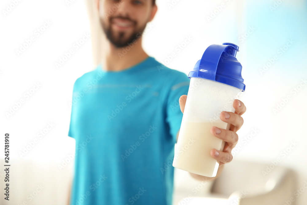 Wall mural Young man with bottle of protein shake at home, closeup