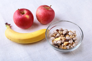 Healthy breakfast with banana, apple and Fresh granola, muesli in bowl on textile background. Top view.