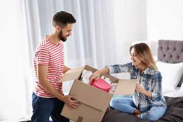 Fototapeta na wymiar Young couple opening parcel in bedroom at home