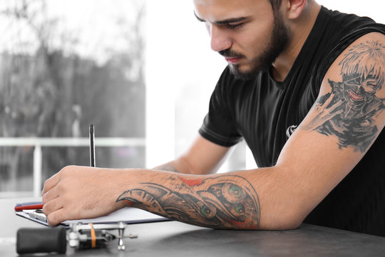 Professional tattoo artist drawing sketch at table indoors