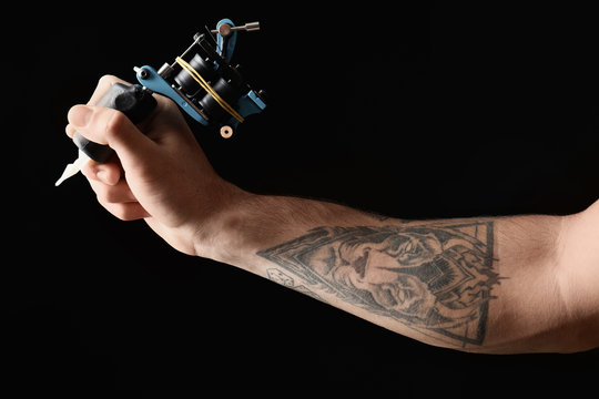 Professional tattoo artist with machine on black background, closeup