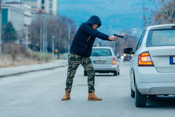 Gangster with a gun trying to rob a guy which is sitting in his car.