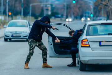 The car thief is pulling the car owner out of his car and trying to get the car while pointing a...