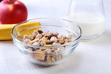Healthy breakfast. Fresh granola, muesli with coconut, banana apple and nuts with milk in a white bowl on textile background. Top view.