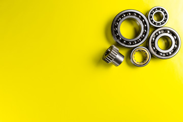 Ball bearing lying on a yellow background with copy space on the left side. Flat view from above.