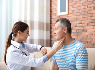 Doctor checking mature man's pulse with fingers at home