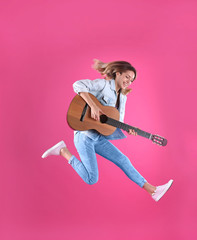 Young woman playing acoustic guitar on color background