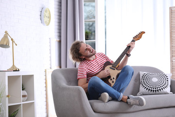 Young man playing electric guitar in living room. Space for text
