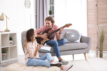 Young man with electric guitar and his girlfriend composing song in living room