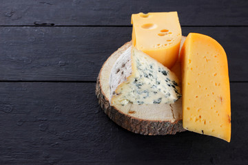 Hard cheese and blue cheese on wooden stand. Different types of cheese on black boards. Swiss cheese and dorblu on dark background
