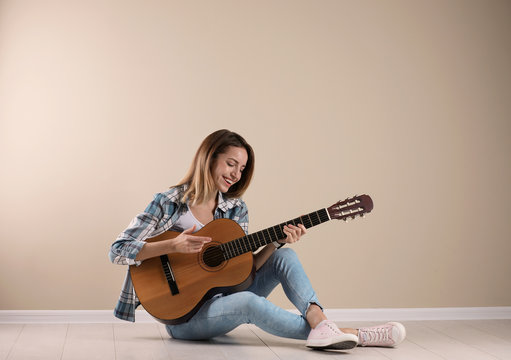 Young woman playing acoustic guitar near grey wall