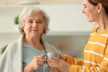 Female caregiver and elderly woman with cup of tea in kitchen