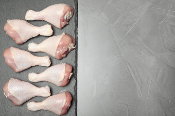 Slate plate with raw chicken drumsticks and space for text on gray background, top view. Fresh meat