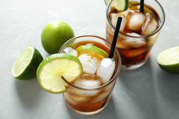 Glasses of cocktail with cola, ice and cut lime on light background