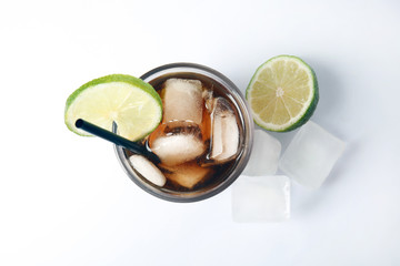 Glass of cocktail with cola, ice and cut lime on white background, top view