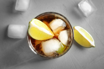 Fototapeta na wymiar Glass of cocktail with cola, ice and cut lime on light background, flat lay