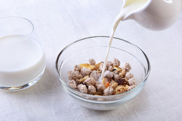 Healthy breakfast. Fresh granola, muesli with coconut, banana apple and nuts with milk in a white bowl on textile background. Top view.