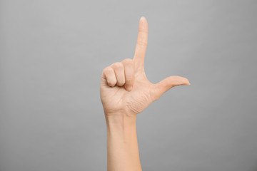 Woman showing L letter on grey background, closeup. Sign language