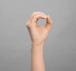 Woman showing O letter on grey background, closeup. Sign language