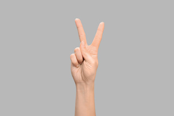 Woman showing V letter on grey background, closeup. Sign language