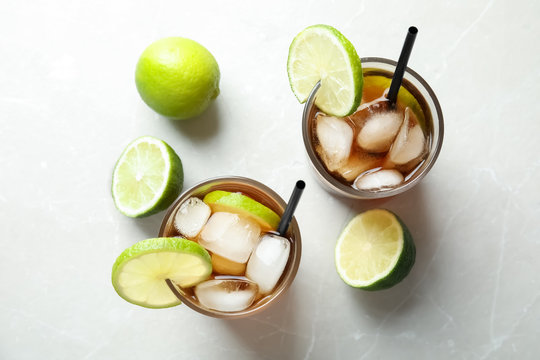 Glasses of cocktail with cola, ice and cut lime on light background, flat lay
