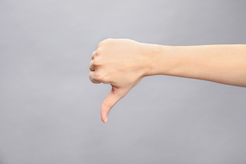 Woman showing thumb down sign on grey background, closeup. Body language