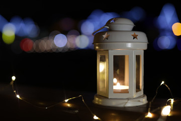 Lantern and Christmas lights on wooden railing outdoors against blurred background, space for text....