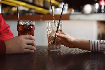 Couple with glasses of  cola at table indoors, closeup. Pouring refreshing beverage