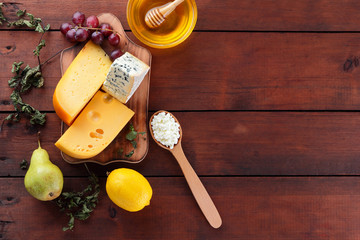 Hard cheese, blue cheese and cottage cheese on wooden board. Different types of cheese and honey on wooden background. Dairy products, pear, lemon and grapes. Top view