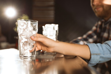 Fototapeta na wymiar Woman holding glass with ice cubes for cola at bar counter