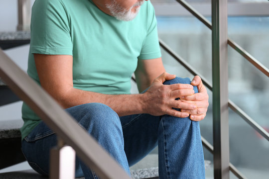 Senior man suffering from knee pain indoors, closeup