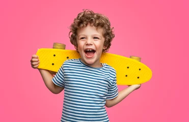 Zelfklevend Fotobehang Gelukkige krullende jongen die lacht en skateboard vasthoudt © kegfire