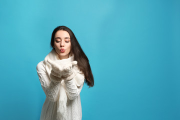 Young woman wearing warm clothes on color background, space for text. Winter season