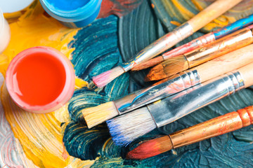 Fototapeta premium Different brushes and jars with paint on palette, top view