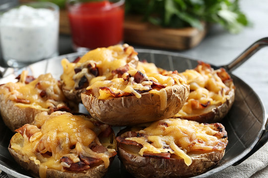 Frying pan of baked potatoes with cheese and bacon on table, closeup