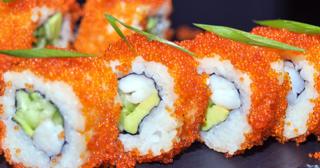 Sushi rolls closeup. Japanese food in restaurant. California sushi roll set with salmon, eel, vegetables and flying fish caviar. On black slate background