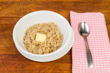 Butter melting in bowl of old fashioned oatmeal with spoon and pink gingham napkin